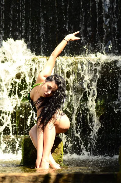 Young brunette model posing against a waterfall