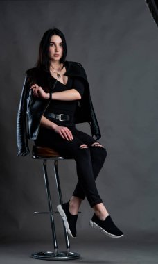 Karanlık stüdyoda şık giyinmiş esmer bir kadın poz veriyor.  