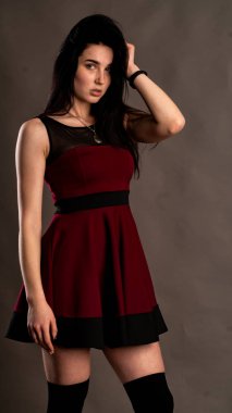 Koyu renk saçlı, kırmızı elbiseli, karanlık stüdyoda poz veren genç ve seksi bir kadın..