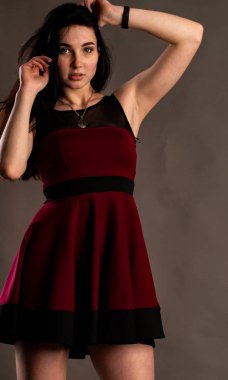 Koyu renk saçlı, kırmızı elbiseli, karanlık stüdyoda poz veren genç ve seksi bir kadın..