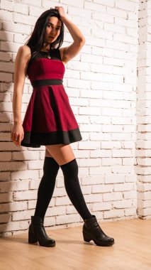 Koyu renk saçlı, kırmızı elbiseli, karanlık stüdyoda poz veren genç ve seksi bir kadın..