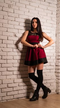 Koyu renk saçlı, kırmızı elbiseli, karanlık stüdyoda poz veren genç ve seksi bir kadın..