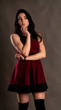 Koyu renk saçlı, kırmızı elbiseli, karanlık stüdyoda poz veren genç ve seksi bir kadın..