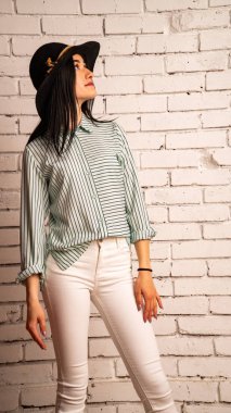 Uzun bacaklı, beyaz tuğla duvar arkasında poz veren genç hippi kadın.