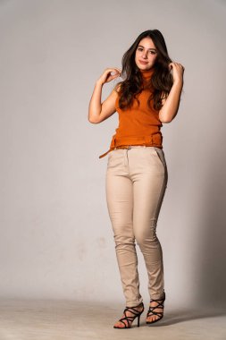 Güzel esmer manken şık kıyafetler içinde, aydınlık odada poz veriyor. 