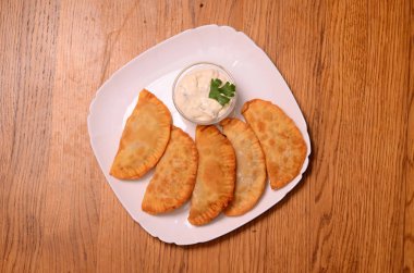 Özbek Doğu Tatar mutfağı, et ve suluguni ile cheburek peynirli sebze ve Yeşiller ahşap bir masa üzerinde beyaz bir tabak içinde.