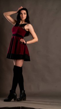 Karanlık stüdyoda şık giyinmiş esmer bir kadın poz veriyor.  