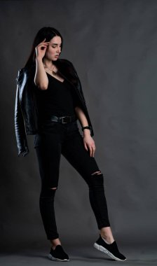 Karanlık stüdyoda şık giyinmiş esmer bir kadın poz veriyor.  