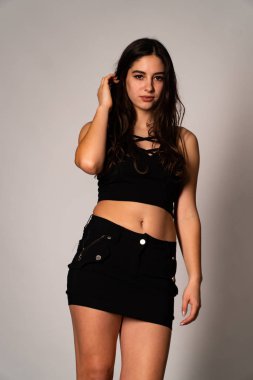 Siyah elbiseli, siyah saçlı, açık renk stüdyo arka planında poz veren güzel bir kadın. 