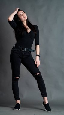 Yüksek tahta koltukta bacak bacak üstüne atmış esmer bir kadının portresi. Geniş paçalı pantolon giyen şık bir kız. Gri arkaplanda stüdyo çekimi