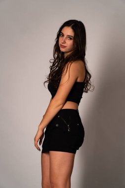 Siyah elbiseli, siyah saçlı, açık renk stüdyo arka planında poz veren güzel bir kadın. 