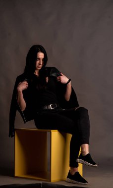 Karanlık stüdyoda şık giyinmiş esmer bir kadın poz veriyor.  