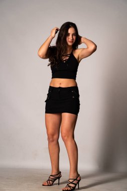 Siyah elbiseli, siyah saçlı, açık renk stüdyo arka planında poz veren güzel bir kadın. 