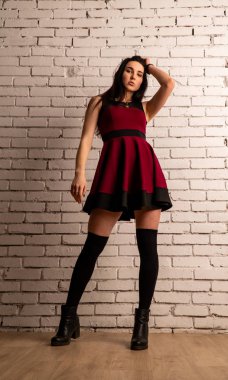 Koyu renk saçlı, kırmızı elbiseli, karanlık stüdyoda poz veren genç ve seksi bir kadın..