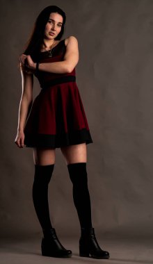 Karanlık stüdyoda şık giyinmiş esmer bir kadın poz veriyor.  