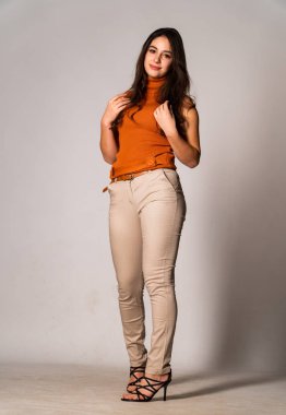 Güzel esmer manken şık kıyafetler içinde, aydınlık odada poz veriyor. 