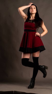 Koyu renk saçlı, kırmızı elbiseli, karanlık stüdyoda poz veren genç ve seksi bir kadın..