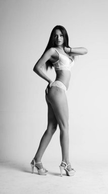 Beyaz iç çamaşırlı ve yüksek topuklu bir kız beyaz arka planda poz veriyor.. 