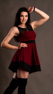 Karanlık stüdyoda şık giyinmiş esmer bir kadın poz veriyor.  