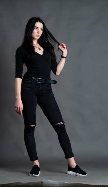 Yüksek tahta koltukta bacak bacak üstüne atmış esmer bir kadının portresi. Geniş paçalı pantolon giyen şık bir kız. Gri arkaplanda stüdyo çekimi