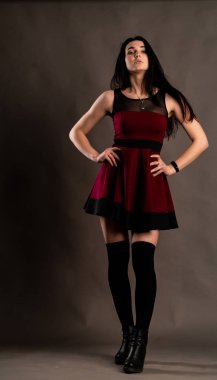 Karanlık stüdyoda şık giyinmiş esmer bir kadın poz veriyor.  