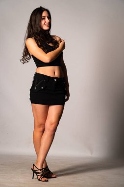 Siyah elbiseli, siyah saçlı, açık renk stüdyo arka planında poz veren güzel bir kadın. 