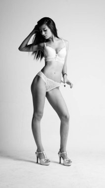 Beyaz iç çamaşırlı ve yüksek topuklu bir kız beyaz arka planda poz veriyor.. 