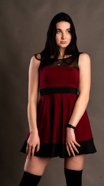 Koyu renk saçlı, kırmızı elbiseli, karanlık stüdyoda poz veren genç ve seksi bir kadın..