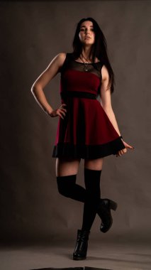 Karanlık stüdyoda şık giyinmiş esmer bir kadın poz veriyor.  