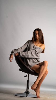 Güzel seksi kız, kısa gri bir elbise, beyaz bir arka plan sandalyesi