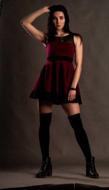 Karanlık stüdyoda şık giyinmiş esmer bir kadın poz veriyor.  