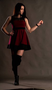 Karanlık stüdyoda şık giyinmiş esmer bir kadın poz veriyor.  