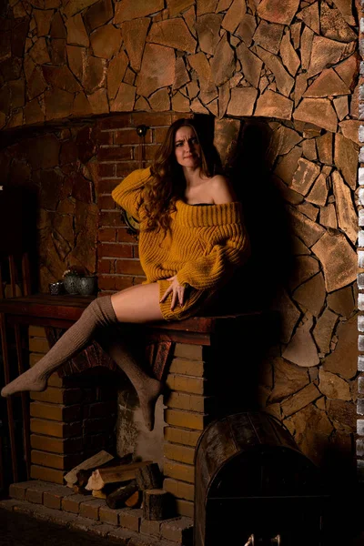 Hermosa chica sentada junto a la chimenea. Interior de lujo decorado para Navidad con ramas de abeto y juguetes —  Fotos de Stock