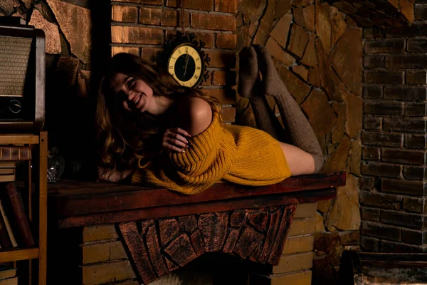 Hermosa chica sentada junto a la chimenea. Interior de lujo decorado para Navidad con ramas de abeto y juguetes —  Fotos de Stock