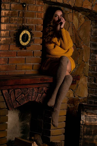 Όμορφο κορίτσι κάθεται δίπλα στο τζάκι. Πολυτελές εσωτερικό διακοσμημένο για τα Χριστούγεννα με κλαδιά ελάτης και παιχνίδια — Φωτογραφία Αρχείου