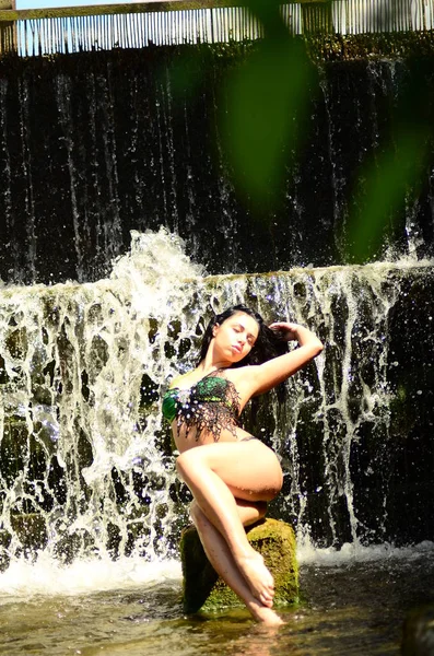 Young brunette model posing against a waterfall