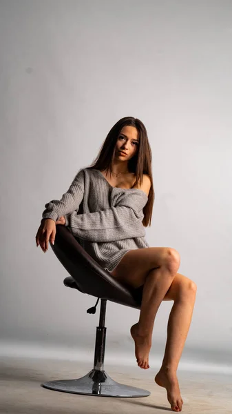 Hermosa chica sexy, con un vestido gris corto, una silla de fondo blanca. — Foto de Stock