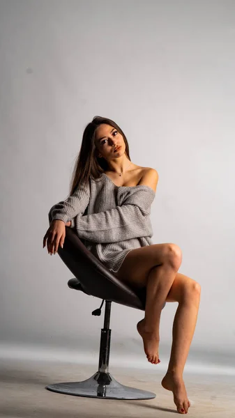 Vacker sexig tjej, poserar en kort grå klänning, en vit bakgrund stol — Stockfoto