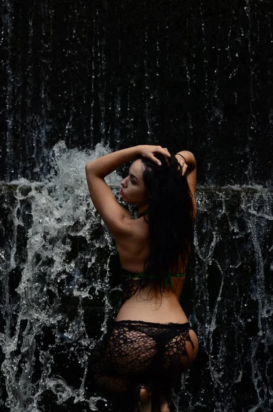 Young brunette model posing against a waterfall