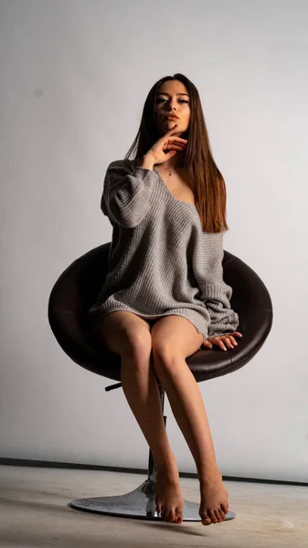 Gyönyörű szexi lány, pózol egy rövid szürke ruha, egy fehér háttér szék — Stock Fotó