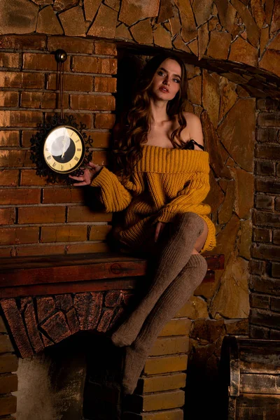 Hermosa chica sentada junto a la chimenea. Interior de lujo decorado para Navidad con ramas de abeto y juguetes —  Fotos de Stock