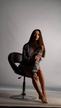 Güzel seksi kız, kısa gri bir elbise, beyaz bir arka plan sandalyesi