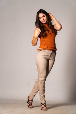 Güzel esmer manken şık kıyafetler içinde, aydınlık odada poz veriyor. 