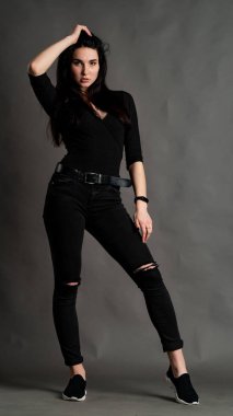 Yüksek tahta koltukta bacak bacak üstüne atmış esmer bir kadının portresi. Geniş paçalı pantolon giyen şık bir kız. Gri arkaplanda stüdyo çekimi