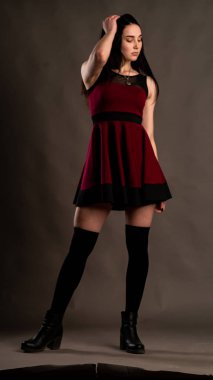 Karanlık stüdyoda şık giyinmiş esmer bir kadın poz veriyor.  