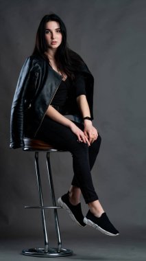 Karanlık stüdyoda şık giyinmiş esmer bir kadın poz veriyor.  