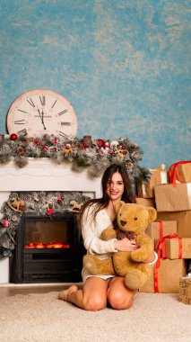 Noel süslemeli stüdyoda şöminenin yanında poz veren çekici esmer kadın.  