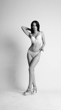 Beyaz iç çamaşırlı ve yüksek topuklu bir kız beyaz arka planda poz veriyor.. 