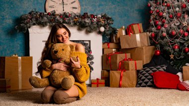 Noel süslemeli stüdyoda şöminenin yanında poz veren güzel esmer genç bir kadın. 