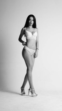 Beyaz iç çamaşırlı ve yüksek topuklu bir kız beyaz arka planda poz veriyor.. 